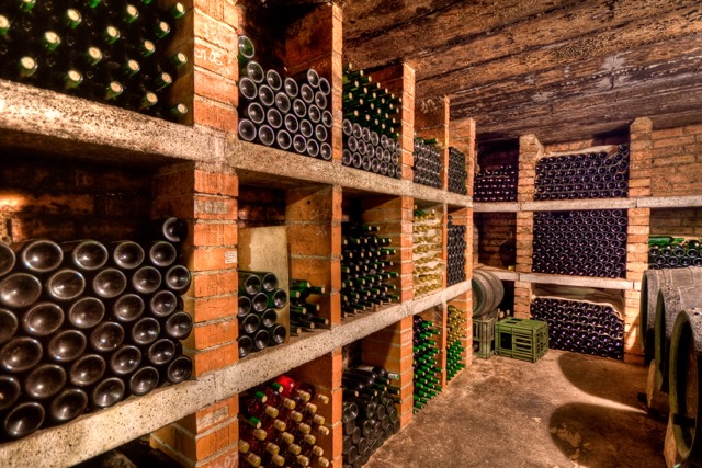 Wine bottles stored horizontally on wooden racks in a dark cellar so their corks stay moist and sealed.