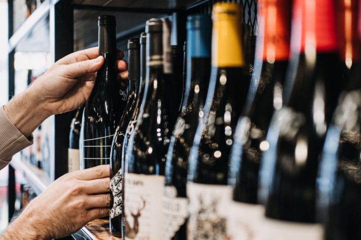 Seorang pembeli sedang memilih sebotol wine dari rak yang dipenuhi botol-botol wine di sebuah toko.