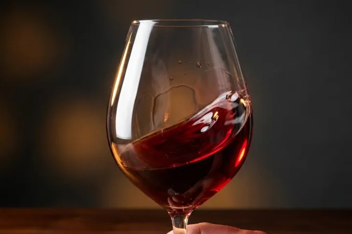 A hand swirling a glass of red wine by the stem to release its aromas during a wine tasting.