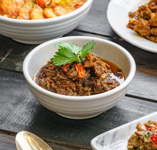 Sepiring rendang daging khas Indonesia disajikan di atas meja makan tradisional.