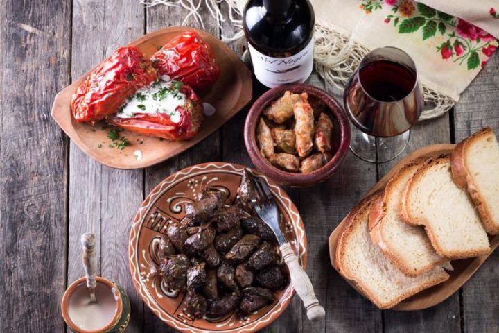 Traditional Moldovan dishes - stuffed peppers, sarmale and grilled meats - served with a bottle and glass of red wine.