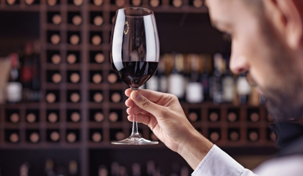 Seorang sommelier sedang mencicipi wine dari gelas untuk menilai aroma dan rasanya.